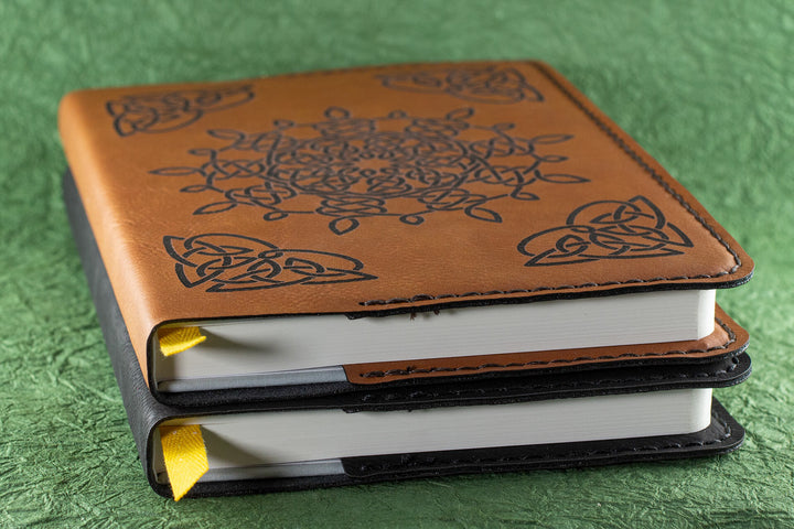 A side photo of two leather-bound journals, one in brown leather and one in black leather, both on a green background.