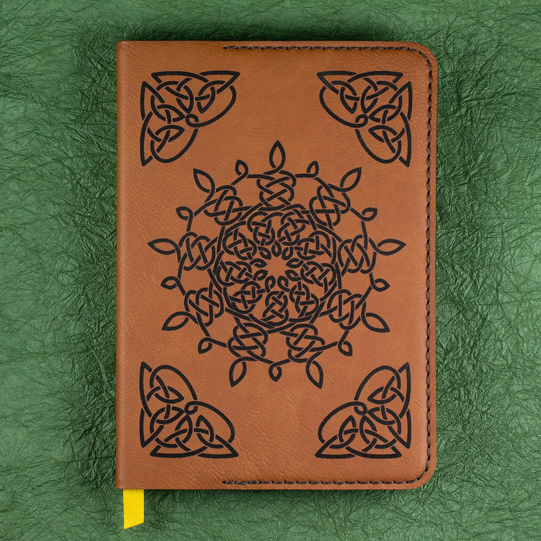 A brown leather journal with a black Celtic pattern, a yellow ribbon bookmark, sitting on a green background..