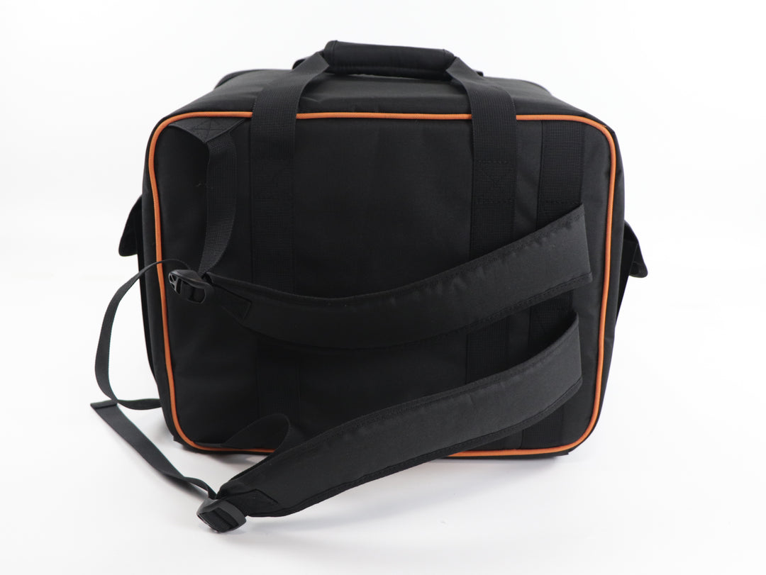 A back view of a black carry bag and backpack with orange trim, with carrying handles on the top and backpack straps running sidewides.