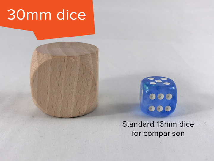 A blank, unfinished wooden die sitting next to a blue and white D6 die. The photo is labelled "30mm dice" in the top left, and "standard 16mm dice for comparison" under the blue die. The wooden die is significantly larger then the blue die.