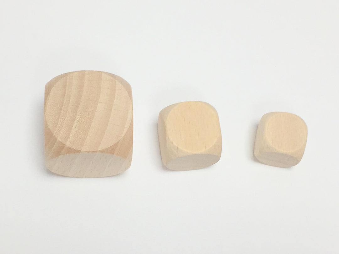 A photo of three, blank, unfinished wooden dice, in three different sizes: large, medium, and small, from left to right.