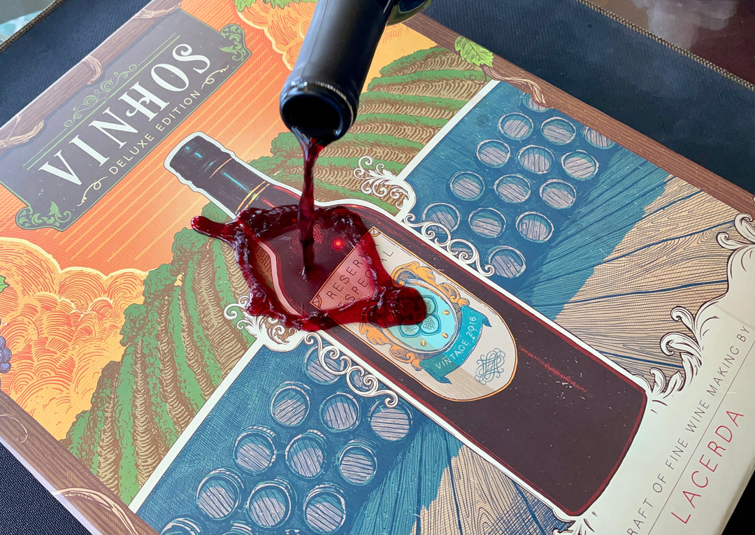 A photo of red wine getting poured on the front cover of the board game Vinhos.