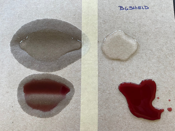 An overhead photo of a side-by-side comparison of two cardboard surfaces with two liquids on top: one clear and one red. The left sample shows the liquids sinking in and getting absorbed into the cardboard. The right side is labeled "BGShield" and shows the two liquids suspended on the top of the cardboard.