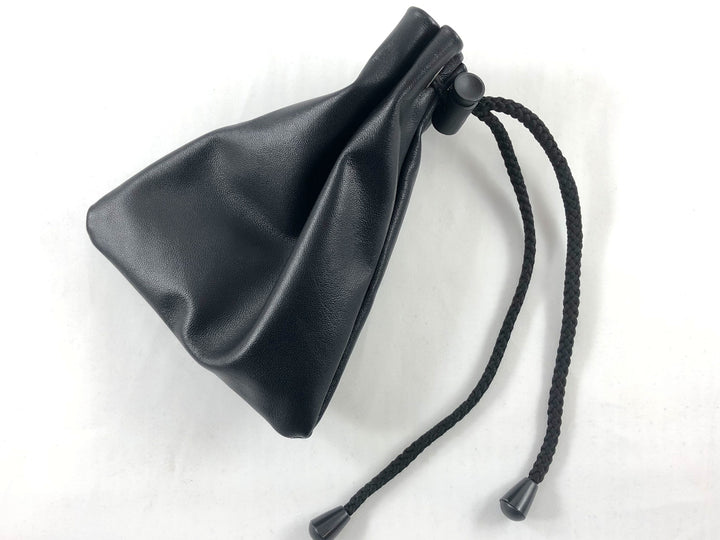 A black leather bag cinched shut with a black drawstring and plastic clasp, laying on a white background.