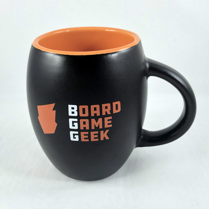A barrel-shaped, matte black coffee mug, with orange on the inside, labeled with "BoardGameGeek" on the outside, and on a white background.