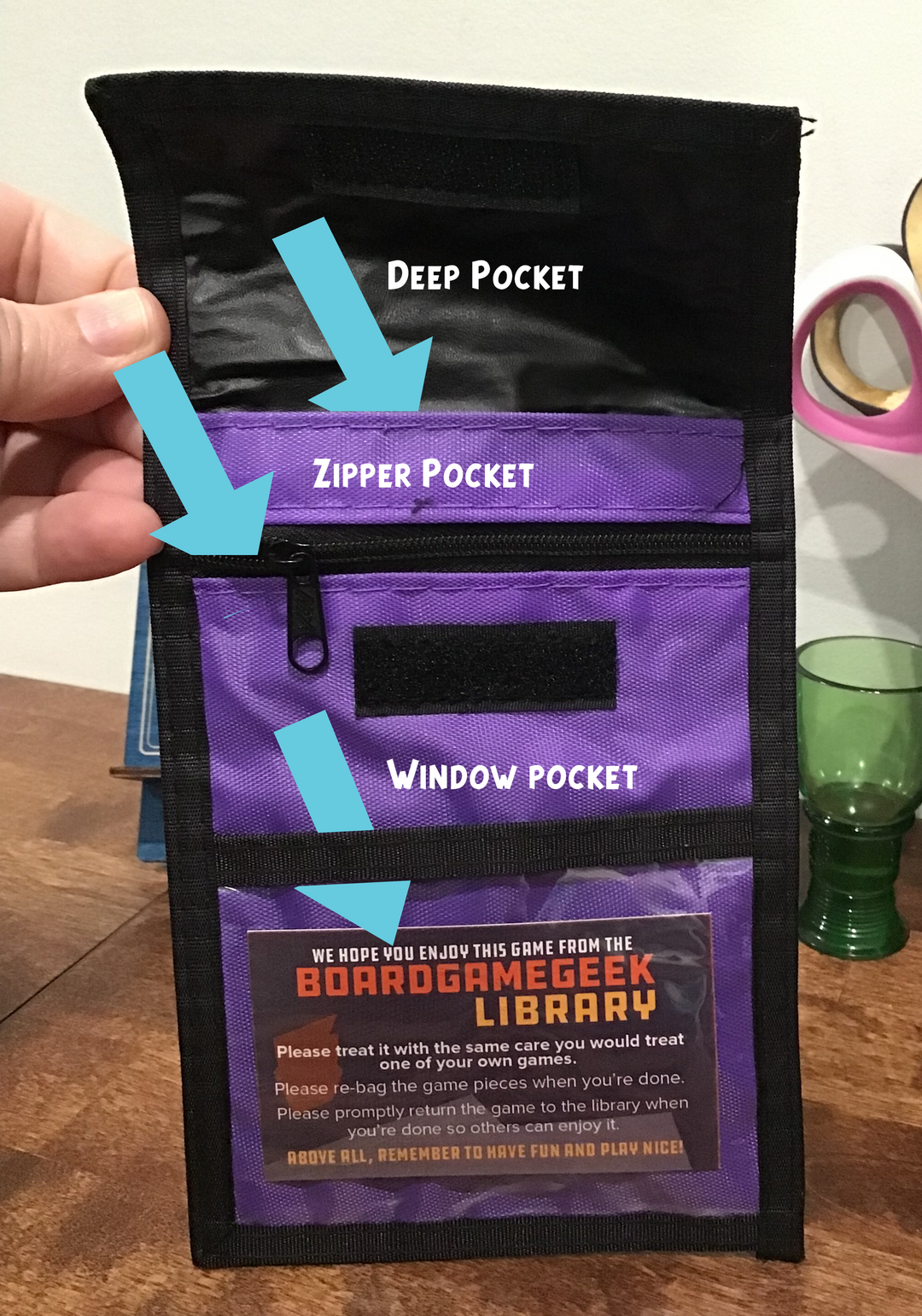 An annotated photo of a purple neck wallet, with three labeled sections titled "Deep Pocket", "Zipper Pocket", and "Window Pocket" and a blue arrow pointing to each.