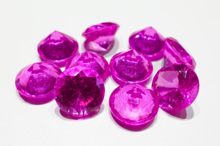 A photo of 10 fuchsia, transparent plastic gems on a white background.