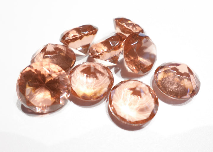 A photo of 10 rose colored, transparent plastic gems on a white background.